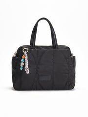Bolso shopper negro acolchado con asas cortas y bandolera larga ajustable, decorado con un llavero de cuentas de colores.