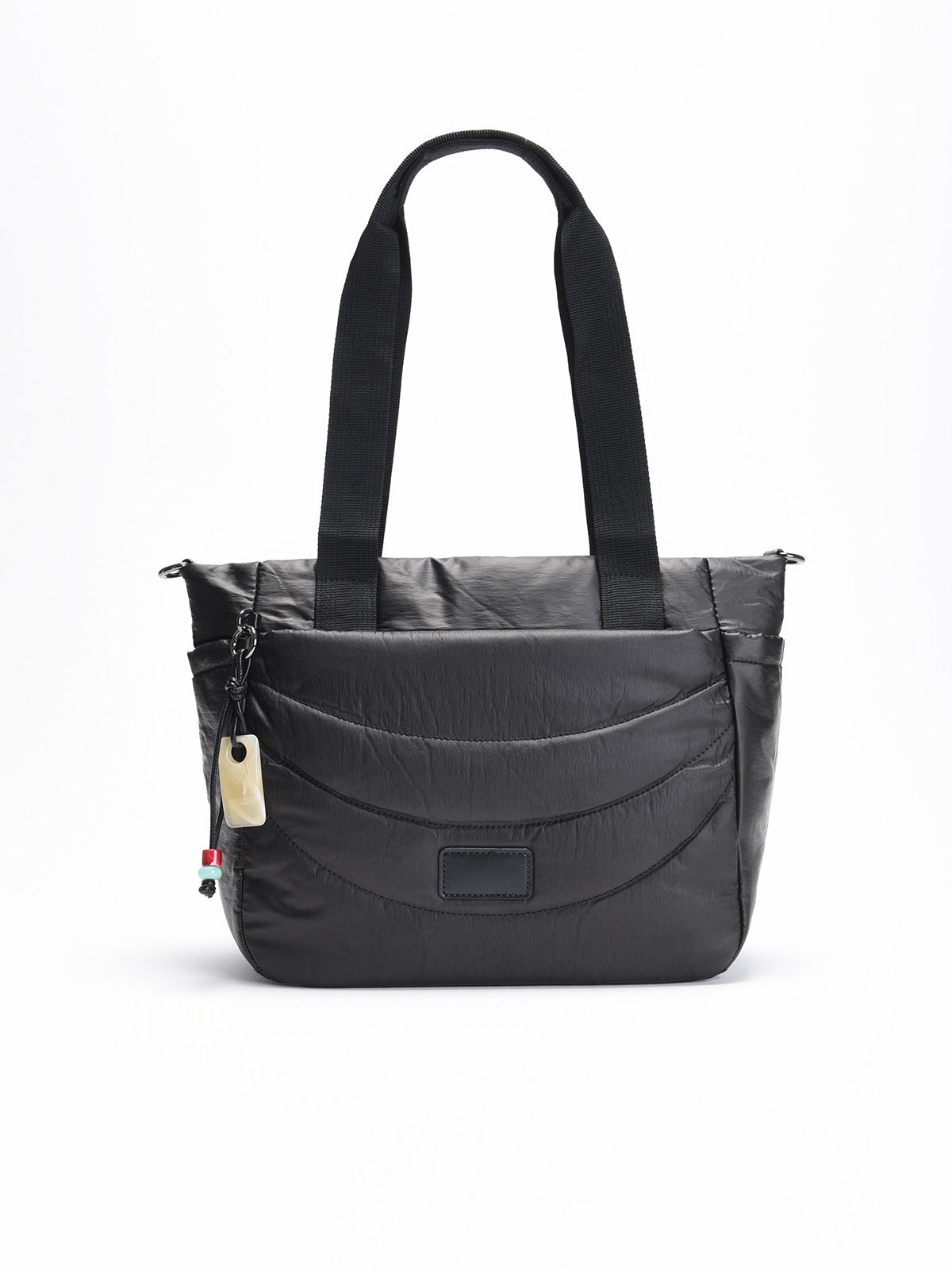 Bolso shopper acolchado negro con asas largas, correa bandolera ajustable y detalle decorativo colgante lateral.