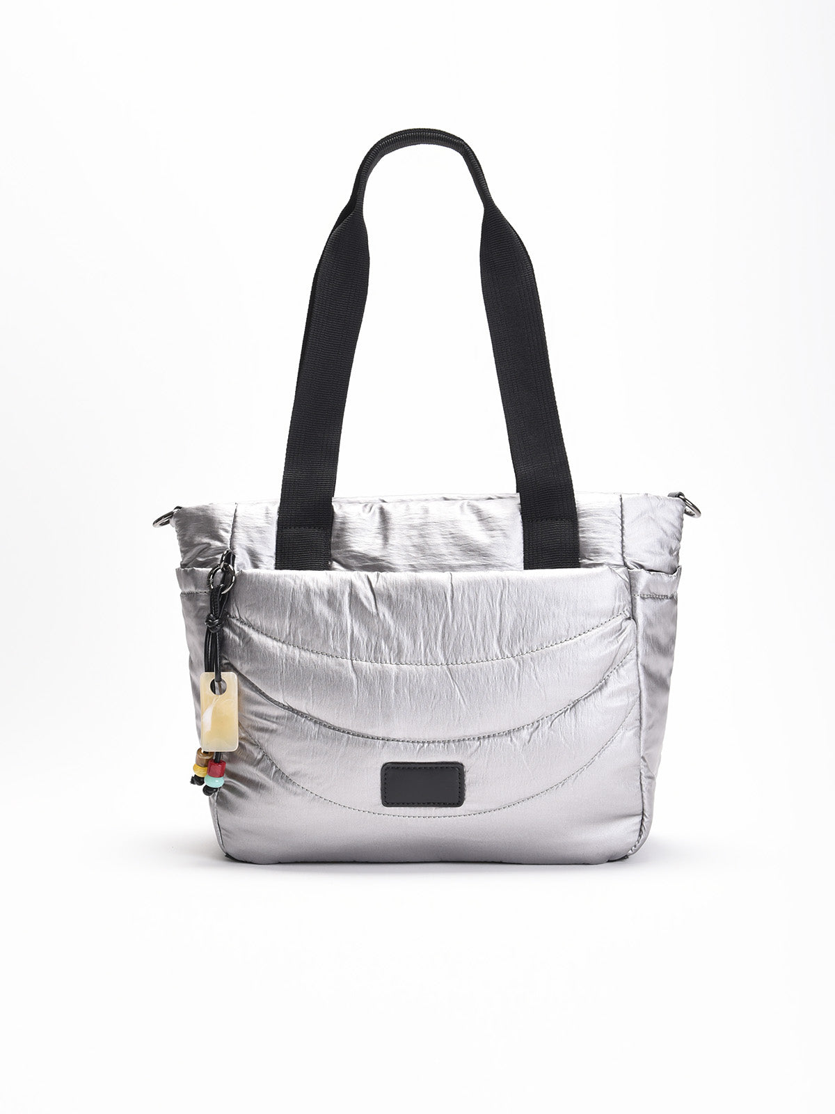 Bolso shopper acolchado plateado con asas negras, correa bandolera ajustable y detalle decorativo colgante en un lateral.